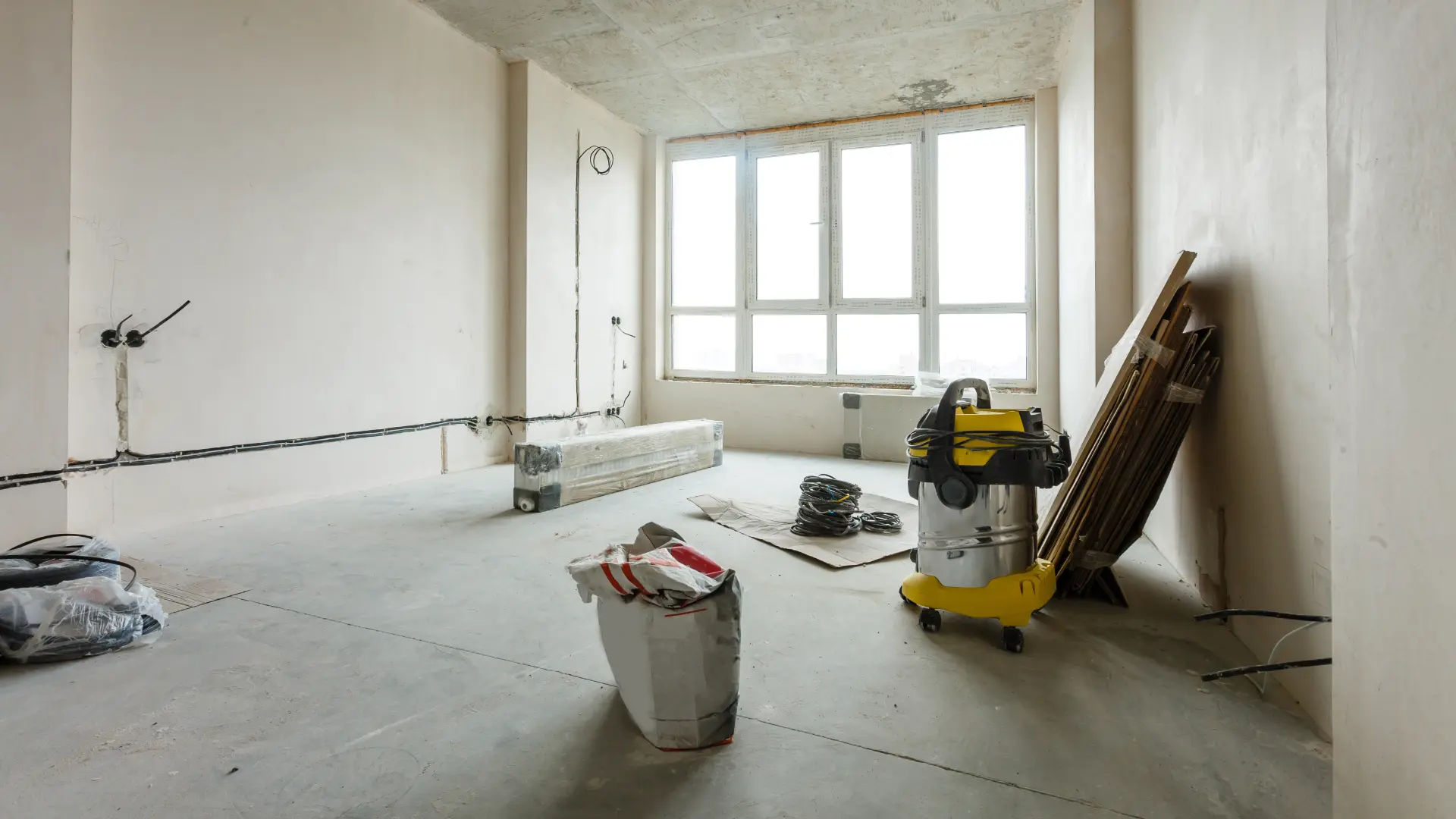 Interior commercial build-out space under construction with finished concrete floors, large windows, and building materials