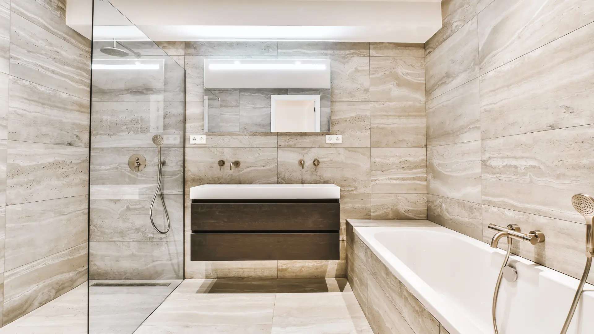 Elegant master bathroom with marble tile, glass shower, freestanding tub, and modern vanity lighting